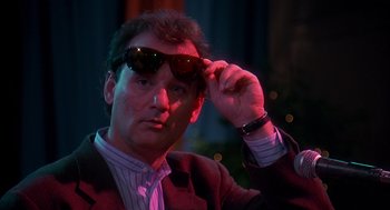 Movie still from “Groundhog Day” (1993), directed by Harold Ramis – A man in a suit and sunglasses looking at the camera; Close Up shot, Over the shoulder angle