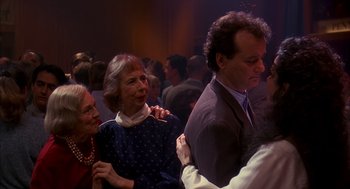 Movie still from “Groundhog Day” (1993), directed by Harold Ramis – A group of people standing around each other at an event; Medium shot, Over the shoulder angle