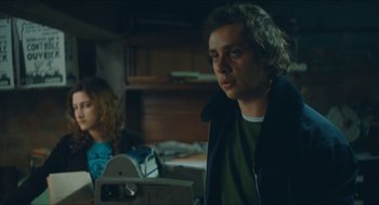 Movie still from “Something in the Air” (2012), directed by Olivier Assayas – A man and a woman are sitting in a dark room; Medium shot, Low angle