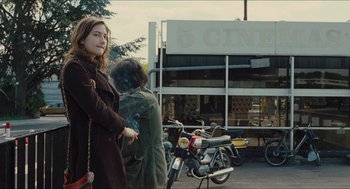 Movie still from “Something in the Air” (2012), directed by Olivier Assayas – A woman standing on the side of the street smoking a cigarette; Medium shot, Over the shoulder angle