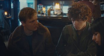 Movie still from “Something in the Air” (2012), directed by Olivier Assayas – Two young men sitting at a table in front of a bar; Medium shot, Over the shoulder angle