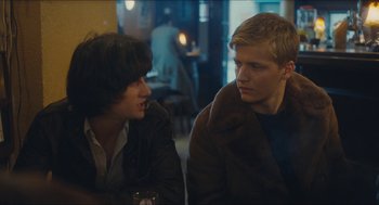 Movie still from “Something in the Air” (2012), directed by Olivier Assayas – Two young men sitting next to each other at a table; Medium shot, Over the shoulder angle