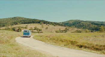 Movie still from “Something in the Air” (2012), directed by Olivier Assayas – An old blue van driving down a road near a field; Extreme Wide shot, High angle