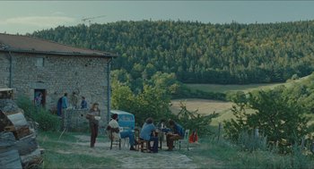 Movie still from “Something in the Air” (2012), directed by Olivier Assayas – A group of people sitting at a table in a field; Extreme Wide shot, High angle