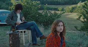 Movie still from “Something in the Air” (2012), directed by Olivier Assayas – Two people sitting on a chair in a field; Medium shot, Over the shoulder angle