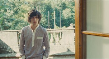 Movie still from “Something in the Air” (2012), directed by Olivier Assayas – A young man standing in front of an open door; Medium shot, Low angle