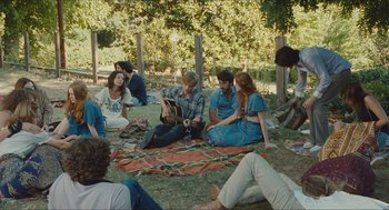 Movie still from “Something in the Air” (2012), directed by Olivier Assayas – A group of people sitting on the ground in the grass; Wide shot, High angle