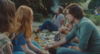 Movie still from “Something in the Air” (2012), directed by Olivier Assayas – A group of people sitting on the ground with a bottle; Medium shot, Over the shoulder angle