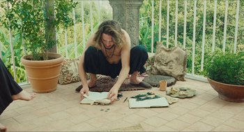 Movie still from “Something in the Air” (2012), directed by Olivier Assayas – A man sitting on the ground reading a book; Wide shot, Overhead angle