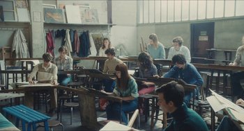 Movie still from “Something in the Air” (2012), directed by Olivier Assayas – A group of people sitting in a room with tables; Wide shot, High angle