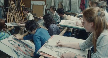 Movie still from “Something in the Air” (2012), directed by Olivier Assayas – A group of people sitting at a table with drawings; Medium shot, High angle