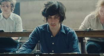 Movie still from “Something in the Air” (2012), directed by Olivier Assayas – A young man sitting in front of a wooden table; Close Up shot, High angle