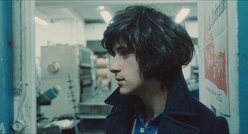Movie still from “Something in the Air” (2012), directed by Olivier Assayas – A young man with long black hair looking to his left; Close Up shot, Over the shoulder angle