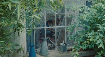 Movie still from “Something in the Air” (2012), directed by Olivier Assayas – A man working in a greenhouse next to plants; Wide shot, High angle