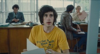 Movie still from “Something in the Air” (2012), directed by Olivier Assayas – A young man sitting at a table in front of other people; Medium shot, Over the shoulder angle
