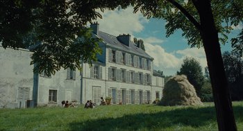Movie still from “Something in the Air” (2012), directed by Olivier Assayas – A group of people sitting in the grass near a building; Extreme Wide shot, Low angle