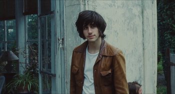 Movie still from “Something in the Air” (2012), directed by Olivier Assayas – A man in a brown leather jacket standing in front of a door; Medium shot, Over the shoulder angle