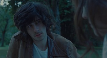 Movie still from “Something in the Air” (2012), directed by Olivier Assayas – A man with long black hair sitting in front of a tree; Close Up shot, Over the shoulder angle