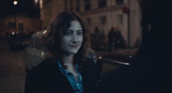 Movie still from “Something in the Air” (2012), directed by Olivier Assayas – A woman with curly hair standing on a city street; Close Up shot, Over the shoulder angle