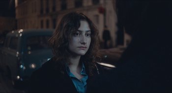 Movie still from “Something in the Air” (2012), directed by Olivier Assayas – A woman with long curly hair standing on the street; Close Up shot, Over the shoulder angle