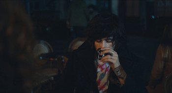 Movie still from “Something in the Air” (2012), directed by Olivier Assayas – A woman with black hair is looking at her cell phone; Medium shot, Over the shoulder angle