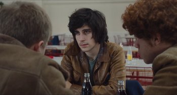 Movie still from “Something in the Air” (2012), directed by Olivier Assayas – A man sitting at a table in a restaurant with a bottle of soda; Close Up shot, Over the shoulder angle