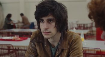 Movie still from “Something in the Air” (2012), directed by Olivier Assayas – A man with long black hair wearing a brown jacket; Close Up shot, Over the shoulder angle