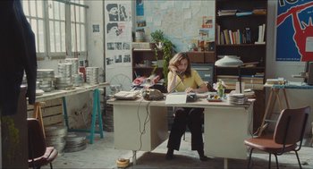 Movie still from “Something in the Air” (2012), directed by Olivier Assayas – A woman sitting at a desk in an office; Wide shot, High angle