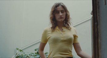 Movie still from “Something in the Air” (2012), directed by Olivier Assayas – A woman in a yellow shirt standing in front of a wall; Medium shot, Low angle