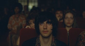 Movie still from “Something in the Air” (2012), directed by Olivier Assayas – A man sitting in a theater with other people in the background; Close Up shot, Over the shoulder angle
