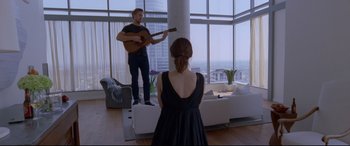 Movie still from “Song to Song” (2017), directed by Terrence Malick – A man and a woman playing a guitar in a living room; Wide shot, Over the shoulder angle