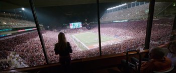 Movie still from “Song to Song” (2017), directed by Terrence Malick – A woman standing in front of a large window looking at a football game; Extreme Wide shot, High angle