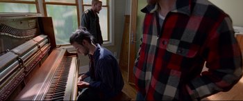 Movie still from “Song to Song” (2017), directed by Terrence Malick – A man sitting at a piano in front of two other men; Medium shot, High angle