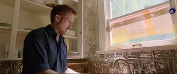 Movie still from “Song to Song” (2017), directed by Terrence Malick – A man sitting at a table in front of a sink; Medium shot, Low angle