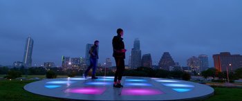 Movie still from “Song to Song” (2017), directed by Terrence Malick – Two men are standing on a dance floor in front of a city skyline at night; Extreme Wide shot, Low angle