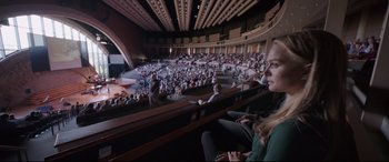Movie still from “Song to Song” (2017), directed by Terrence Malick – A crowd of people sitting and standing in an auditorium; Extreme Wide shot, High angle