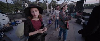 Movie still from “Song to Song” (2017), directed by Terrence Malick – A woman holding a guitar while standing next to two men; Medium shot, Over the shoulder angle