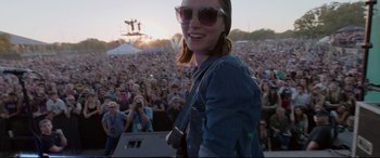 Movie still from “Song to Song” (2017), directed by Terrence Malick – A woman is smiling at a concert while people watch; Medium shot, Over the shoulder angle