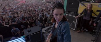 Movie still from “Song to Song” (2017), directed by Terrence Malick – A woman standing in front of a crowd with a microphone; Medium shot, Over the shoulder angle