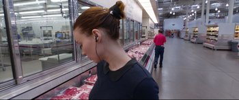 Movie still from “Song to Song” (2017), directed by Terrence Malick – A woman wearing ear buds in a meat market; Close Up shot, Over the shoulder angle