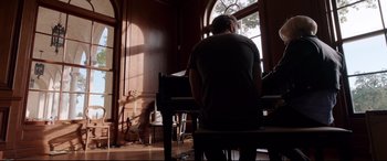 Movie still from “Song to Song” (2017), directed by Terrence Malick – A man sitting in front of a piano in a living room; Wide shot, Low angle