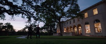 Movie still from “Song to Song” (2017), directed by Terrence Malick – Two people standing in front of a large house; Extreme Wide shot, Low angle