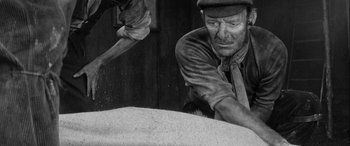 Movie still from “Sons and Lovers” (1960), directed by Jack Cardiff – A man in a hat and a jacket is working on a pile of grain; Medium shot, High angle
