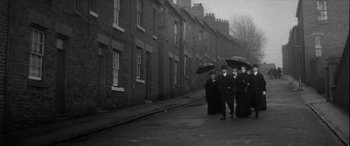 Movie still from “Sons and Lovers” (1960), directed by Jack Cardiff – A group of people walking down a street holding umbrellas; Wide shot, High angle