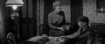 Movie still from “Sons and Lovers” (1960), directed by Jack Cardiff – An older woman standing at a table with a plate of food; Medium shot, Over the shoulder angle