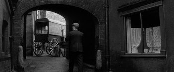 Movie still from “Sons and Lovers” (1960), directed by Jack Cardiff – A man in a suit and hat standing in front of an archway in an alleyway; Wide shot, Low angle