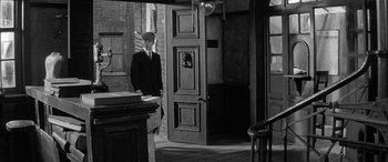 Movie still from “Sons and Lovers” (1960), directed by Jack Cardiff – A black and white photo of a man standing in a doorway; Wide shot, High angle