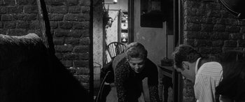 Movie still from “Sons and Lovers” (1960), directed by Jack Cardiff – A woman bending over in a room next to a chair; Medium shot, High angle