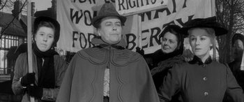 Movie still from “Sons and Lovers” (1960), directed by Jack Cardiff – A man wearing a hat and a cape standing next to a woman; Medium shot, Low angle