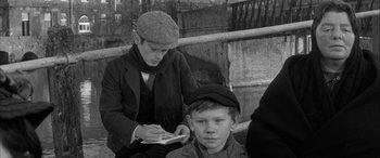Movie still from “Sons and Lovers” (1960), directed by Jack Cardiff – An older woman writing on a piece of paper next to a young boy; Medium shot, High angle